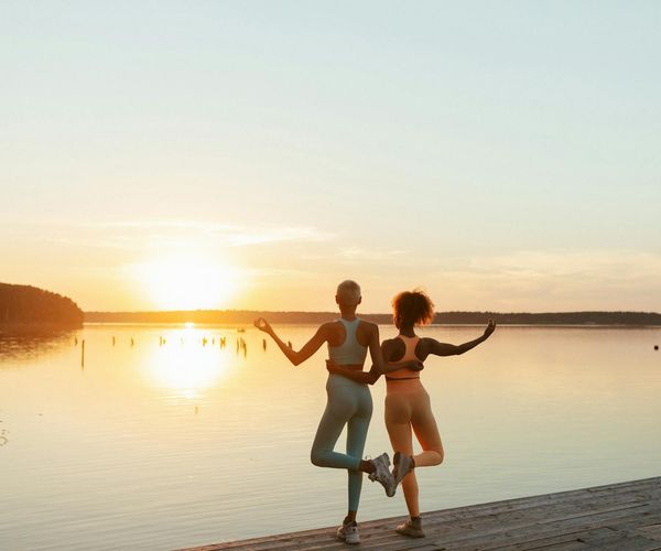 Person meditating peacefully outdoors by a calm lake at sunrise.